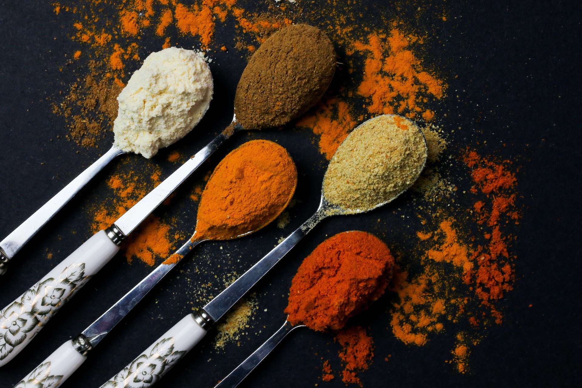 Photo of classic Indian spices displayed on spoons against a black background